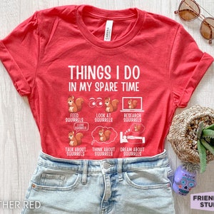 May include: Red t-shirt with the text "Things I do in my spare time" and illustrations of squirrels. The text below the squirrels includes phrases like "Feed squirrels", "Look at squirrels", "Research squirrels", "Talk about squirrels", "Think about squirrels", and "Dream about squirrels".