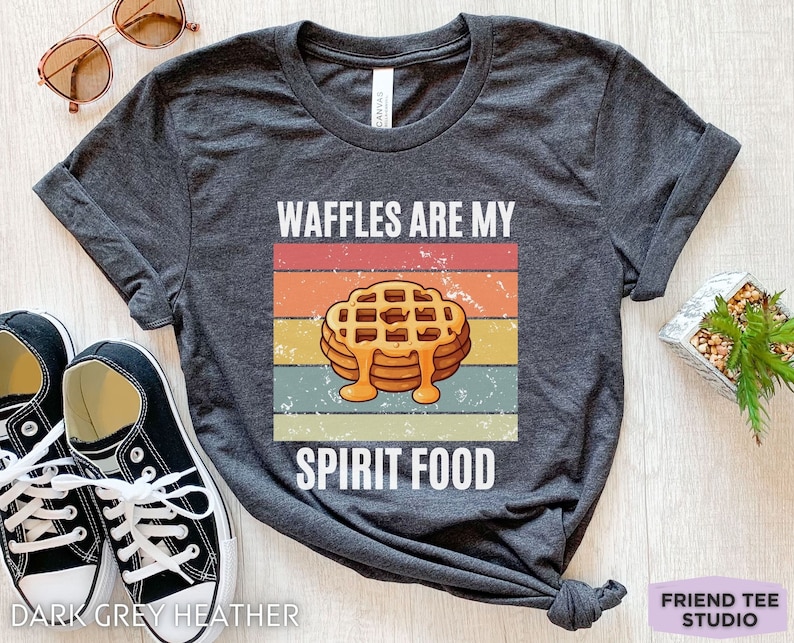 Pu&ograve; includere: T-shirt grigio scuro melange con la scritta "WAFFLES ARE MY SPIRIT FOOD" e una grafica di waffle con sciroppo. Il design presenta una combinazione di colori retr&ograve; ed &egrave; stampato su una maglietta morbida.