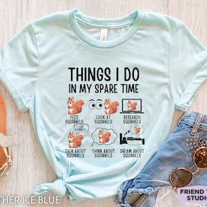 May include: A light blue t-shirt with the text "Things I do in my spare time" and a series of illustrations of squirrels. The illustrations depict squirrels feeding, looking at, researching, talking about, thinking about, and dreaming about squirrels.