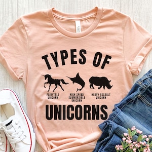 May include: A peach-colored t-shirt with the text "Types of Unicorns" in black. The shirt features three black silhouettes of unicorns: a fairytale unicorn, a high-speed submersible unicorn, and a heavy assault unicorn.