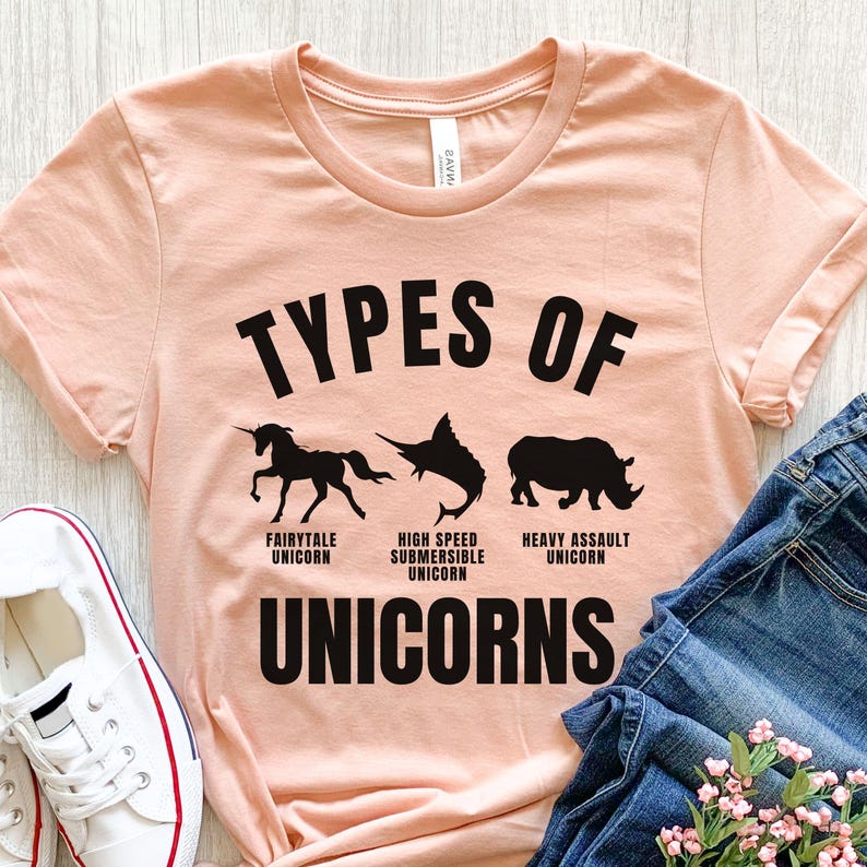 May include: A peach-colored t-shirt with the text "Types of Unicorns" in black. The shirt features three black silhouettes of unicorns: a fairytale unicorn, a high-speed submersible unicorn, and a heavy assault unicorn.