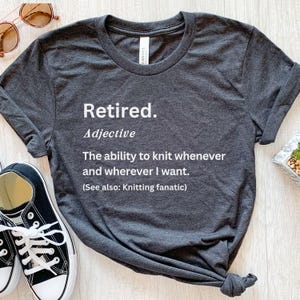 Puede incluir: Camiseta gris oscuro con el texto "Retired. Adjective: The ability to knit whenever and wherever I want. (See also: Knitting fanatic)". La camiseta se combina con zapatillas deportivas en blanco y negro y gafas de sol.