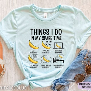 Peut inclure: Un t-shirt bleu clair avec le texte "Things I do in my spare time" et une s&eacute;rie d'illustrations de bananes avec du texte d&eacute;crivant des activit&eacute;s li&eacute;es aux bananes. Le texte comprend "Eat bananas", "Look at bananas", "Research bananas", "Talk about bananas", "Think about bananas", et "Dream about bananas".