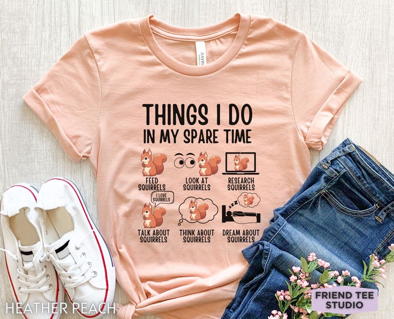 May include: A peach-colored t-shirt with the text "THINGS I DO IN MY SPARE TIME" and a series of illustrations of squirrels with text describing activities related to squirrels. The text includes "FEED SQUIRRELS", "LOOK AT SQUIRRELS", "RESEARCH SQUIRRELS", "TALK ABOUT SQUIRRELS", "THINK ABOUT SQUIRRELS", and "DREAM ABOUT SQUIRRELS".