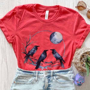 May include: Red t-shirt featuring a watercolor design of three black crows perched on a branch, with a full moon in the background. The shirt is made of a soft material and has a classic crew neck.