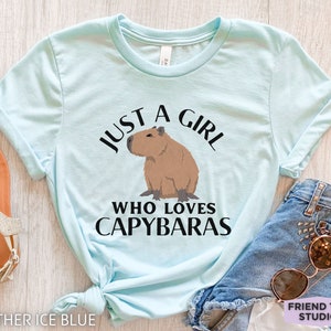 May include: A light blue t-shirt with the text "Just a girl who loves capybaras" and a cartoon image of a capybara.