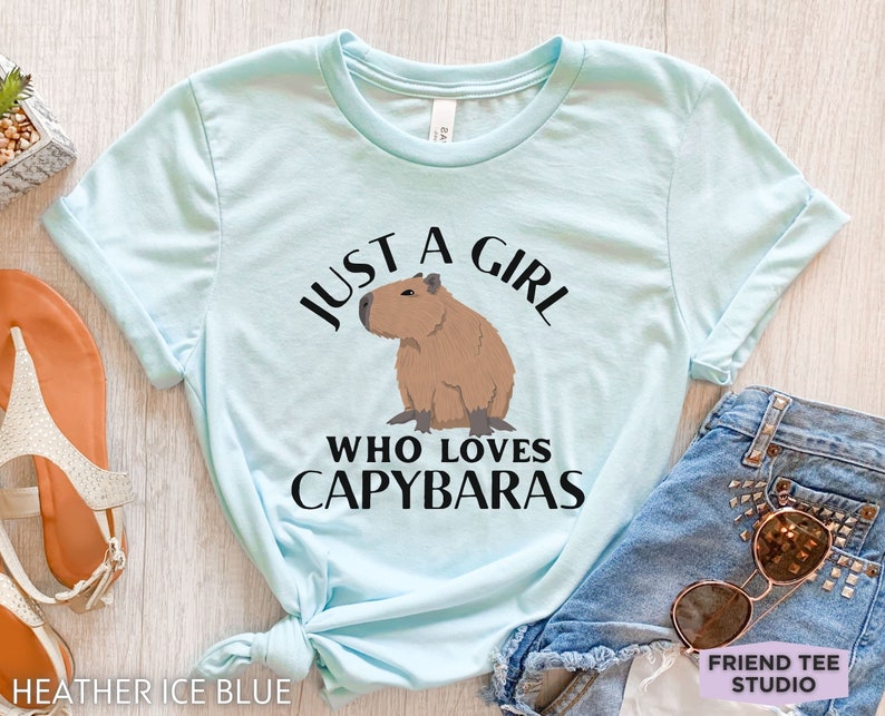 May include: A light blue t-shirt with the text "Just a girl who loves capybaras" and a cartoon image of a capybara.
