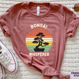 May include: Heather mauve t-shirt with a vintage-style graphic of a bonsai tree and the text "Bonsai Whisperer".