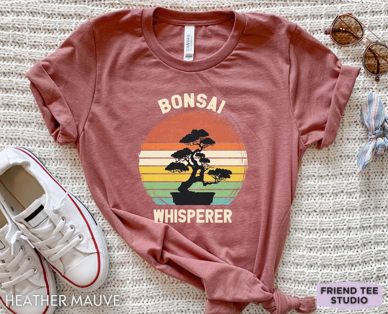 May include: Heather mauve t-shirt with a vintage-style graphic of a bonsai tree and the text "Bonsai Whisperer".