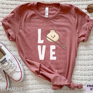 Op de afbeelding: Heather mauve t-shirt met het woord "LOVE" in wit gedrukt. De "O" is vervangen door een cartoon-dumpling met eetstokjes.