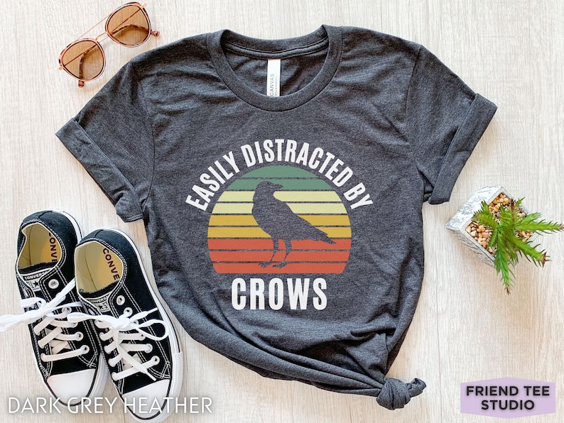 May include: Dark grey heather t-shirt with a vintage sunset graphic and a black crow silhouette. The text "Easily Distracted By Crows" is printed on the shirt.