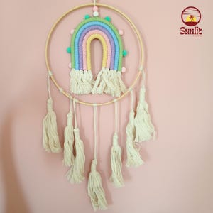 May include: A rainbow-colored macrame wall hanging with a wooden hoop and white tassels. The rainbow is made of yarn and has pom-poms around the edges.