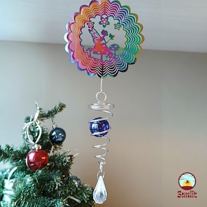Könnte beinhalten: Ein regenbogenfarbener Windfänger aus Metall mit einem Feendesign und einer blauen Glasperle, die an einer silbernen Spirale hängt. Der Windfänger hängt an einer Decke.