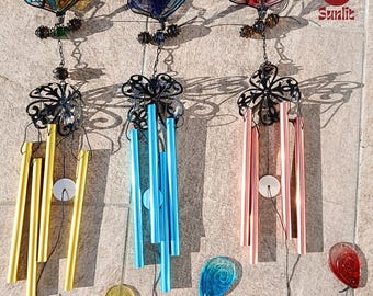 May include: Three wind chimes featuring butterfly designs. The wind chimes are made of metal and have a variety of coloured tubes. The butterflies are made of stained glass and have different colours. The wind chimes are hanging from a ceiling or a tree branch.