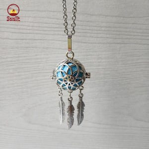 Puede incluir: Collar plateado con un colgante de filigrana en forma de esfera, interior turquesa y tres colgantes de plumas. El colgante cuelga de una fina cadena. El logotipo "Sunlite" está en la esquina superior izquierda.