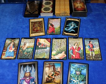 May include: Tarot card spread with 10 cards laid out on a blue surface. The cards are decorated with gold trim and feature various illustrations, including a woman with a crown, a man with a sword, and a mermaid.