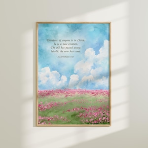 May include: A framed watercolor print featuring a serene landscape. The artwork depicts a blue sky with fluffy white clouds above a field of pink flowers and green grass. The text reads: "Therefore, if anyone is in Christ, he is a new creation..."