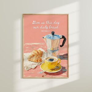 May include: A framed print depicting a breakfast scene with a coffee pot, yellow coffee cup, croissants, and the text "Give us this day our daily bread". The background is a pink and red color. The print is in a wooden frame.