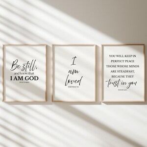 May include: Three framed art prints with inspirational quotes in black script on a white background. The quotes include "Be still and know that I AM GOD", "I am loved", and "You will keep in perfect peace". The frames are light brown.