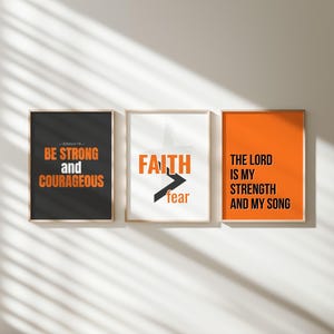 May include: Three framed art prints with inspirational quotes. The first is black with orange text that reads "BE STRONG AND COURAGEOUS." The second is white with "FAITH" and an arrow pointing away from "fear." The third is orange with text.
