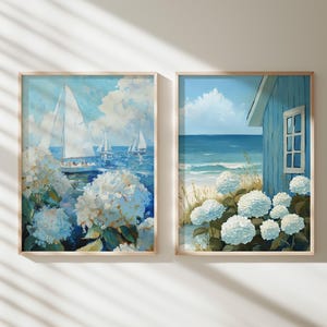 May include: Two framed art prints. One depicts sailboats on a blue sea with white clouds and white flowers. The other shows a blue beach house, ocean, and white flowers. Both have light wood frames.
