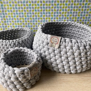 May include: Three gray crocheted baskets of varying sizes. The largest basket has a label that reads "Live 2 Craft".