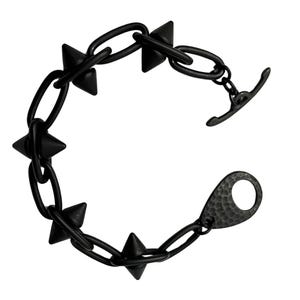 May include: A black bracelet featuring a chain link design with pointed cone-shaped studs. The bracelet has a toggle clasp closure. The jewelry is made of a dark, matte metal.