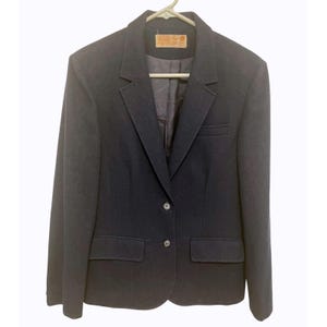 May include: A navy blue blazer with two buttons and two front pockets. The blazer is hanging on a hanger. A label is visible at the top of the blazer.