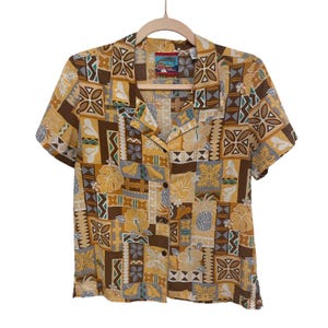 May include: Short-sleeved button-down shirt with a colorful Hawaiian print. The shirt features a repeating pattern of flowers, geometric shapes, and other tropical motifs in shades of yellow, brown, and gray. The shirt is hanging on a wooden hanger.
