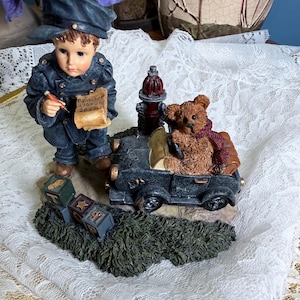 May include: A resin figurine featuring a child in a dark blue uniform and cap writing on a paper labeled "TICKET NEARLY SPEEDING". Beside the child is a dark car with a brown teddy bear in the driver seat, a red fire hydrant, and three alphabet blocks.