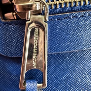 K&ouml;nnte beinhalten: Eine leuchtend blaue Handtasche aus strukturiertem Leder mit einem polierten goldfarbenen Rei&szlig;verschlussanh&auml;nger. Der Anh&auml;nger ist mit dem Text REBECCAMINKOFF graviert. Eine passende blaue Lederlasche ist an der Metallschlie&szlig;e befestigt.