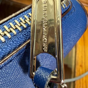 K&ouml;nnte beinhalten: Eine leuchtend blaue, strukturierte Handtasche mit einem polierten, silberfarbenen Metall-Rei&szlig;verschlussanh&auml;nger, der mit dem Text REBECCAMINKOFF graviert ist. Die Tasche hat eine passende blaue Lederlasche und eine silberne Metallkette.