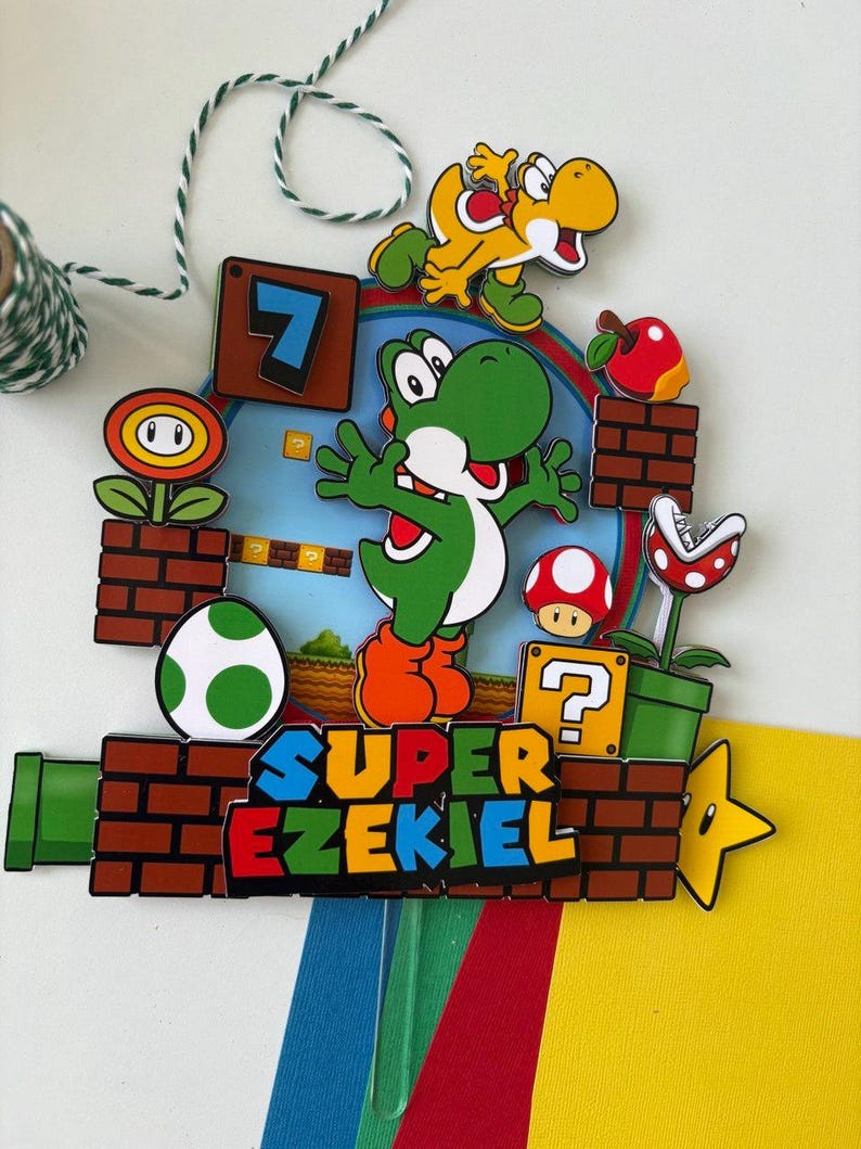 May include: A colorful Super Mario-themed decoration featuring Yoshi, a yellow dinosaur, and other game elements. The design includes a green pipe, brick blocks, a question mark box, and the text "SUPER EZEKIEL".