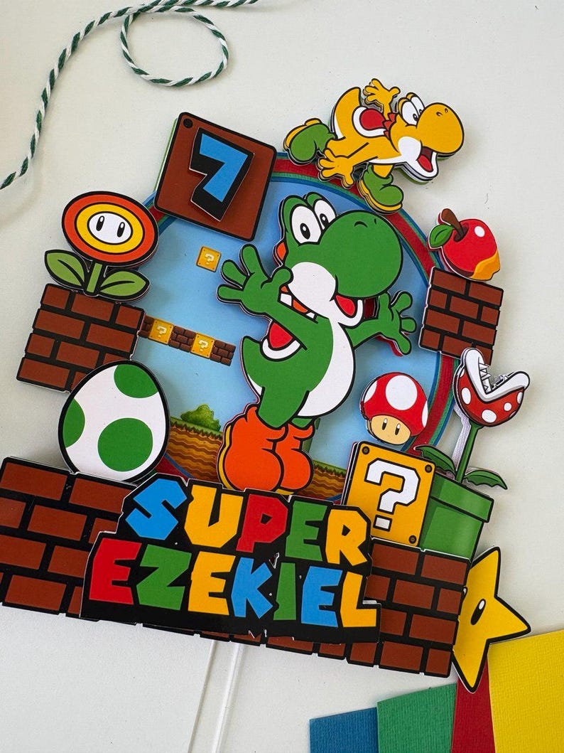May include: A colorful Super Mario-themed cake topper featuring Yoshi, a yellow dinosaur, a red apple, a mushroom, and a Piranha Plant. The topper includes the text "SUPER EZEKIEL" and the number 7. The design is set against a brick background.
