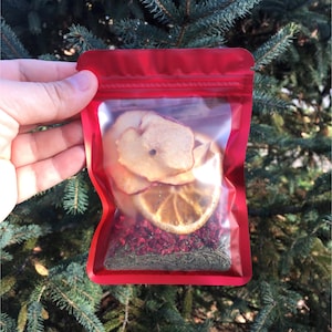 May include: A red resealable pouch filled with dried fruit and herbs for making tea. The pouch contains dried apple slices, orange slices, and red berries.
