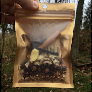 May include: A gold resealable pouch filled with a blend of spices and coffee beans. The pouch is open and the contents are visible. The spices include cinnamon sticks, ginger, and other unidentified spices.