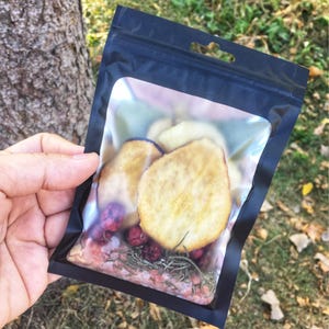 May include: A clear plastic bag with a black zipper closure contains dried fruit and herbs. The bag is filled with dried apple slices, dried cranberries, and dried rosemary sprigs.