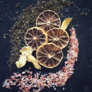 May include: A close-up of dried orange slices with pink Himalayan salt on a dark background. The orange slices are arranged in a circle with the salt scattered around them.