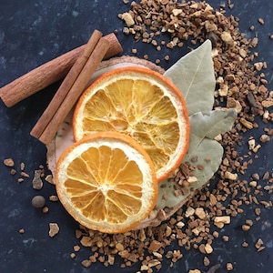 May include: Two dried orange slices on a dark background with cinnamon sticks and brown spices.