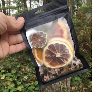 May include: A clear plastic bag filled with dried citrus fruit slices, pink Himalayan salt, and black peppercorns. The bag is sealed and has a black zipper.