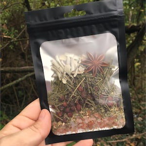 May include: A clear plastic bag filled with a blend of herbs, spices, and salt. The bag is sealed with a black zipper and has a black hang tag. The contents include dried herbs, star anise, and pink Himalayan salt.