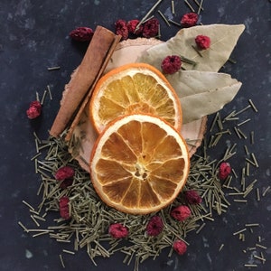 May include: Two dried orange slices with a cinnamon stick and dried cranberries on a dark background. The orange slices are arranged in a circle with the cinnamon stick in the center. The cranberries are scattered around the orange slices.