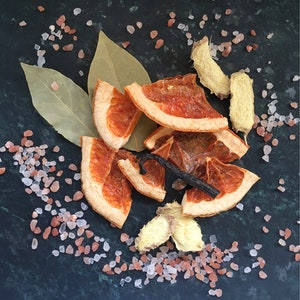 May include: Dried orange slices, bay leaves, ginger, and pink Himalayan salt on a dark green surface.