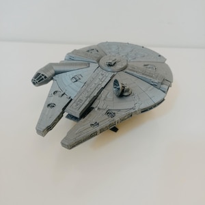 May include: A detailed, grey model of the Millennium Falcon starship. The model features intricate paneling, a cockpit, and various mechanical details. The ship is a recognisable icon from the Star Wars franchise.