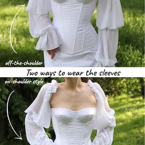 May include: A white corset-style dress with two ways to wear the sleeves. The first option is off-the-shoulder, and the second is on-shoulder style. The sleeves are sheer, with a layered design and ruffled cuffs. The dress has a sweetheart neckline and a fitted bodice.