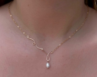 May include: A delicate gold-colored necklace featuring a flowing, asymmetrical design. The necklace has a small, teardrop-shaped pendant with a single, white pearl. The chain is fine and the overall aesthetic is minimalist and elegant.