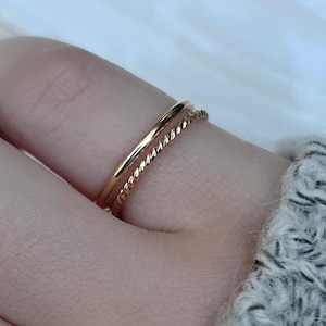 Puede incluir: Dos anillos de oro en un dedo. Un anillo es una banda simple, el otro es una banda retorcida.