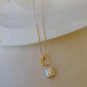 Op de afbeelding: Een gouden ketting met een schuifgesp en een grote, crèmekleurige barokparel hanger.