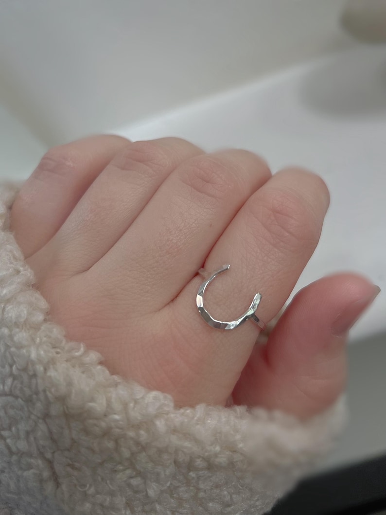 K&ouml;nnte beinhalten: Ein silberner Ring in Form eines Hufeisens. Der Ring ist texturiert und hat eine geh&auml;mmerte Oberfl&auml;che.