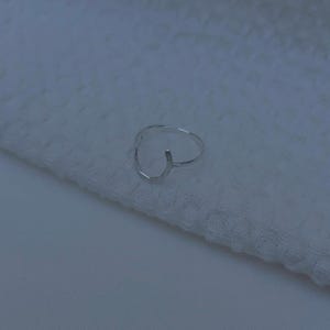 K&ouml;nnte beinhalten: Ein silberner Ring mit geometrischem Design. Der Ring ist an einer Seite offen und hat eine leicht gebogene Form.